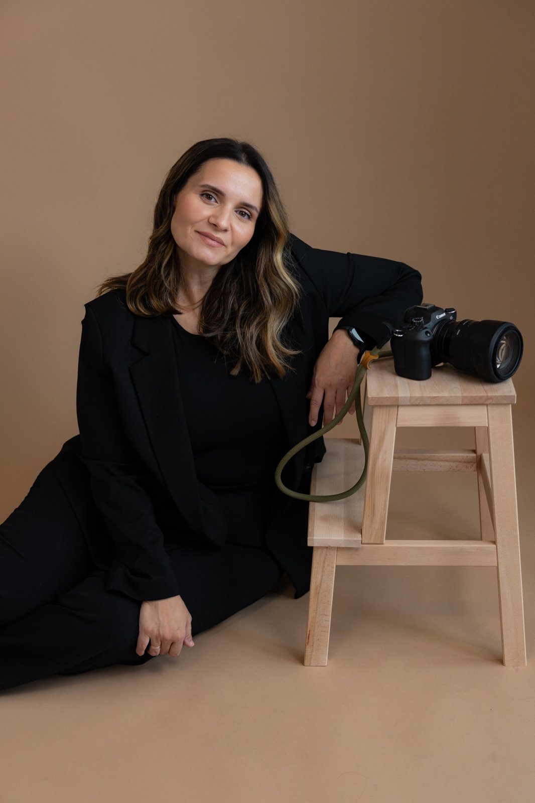 Madalina Leahu sitzt lächelnd neben einem Holzhocker mit ihrer Kamera